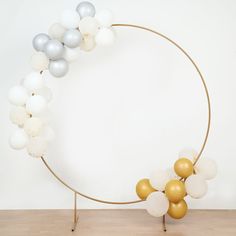 a gold and white balloon garland on a round metal stand in front of a white wall