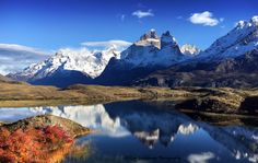 the mountains are covered in snow and fall foliage near a body of water that is surrounded by grass