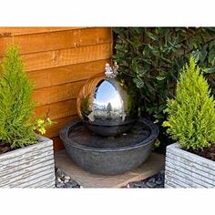 there is a water fountain in the middle of two planters and one has a silver ball on it