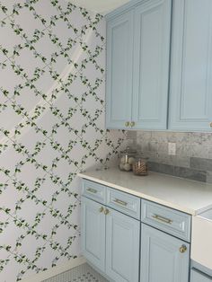 a kitchen with blue cabinets and wallpaper in the backround, next to a white sink