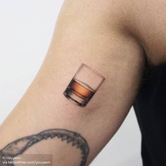 a person with a tattoo on their arm holding up a glass of whiskey and a snake