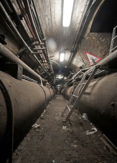 the inside of a tunnel with pipes and ladders