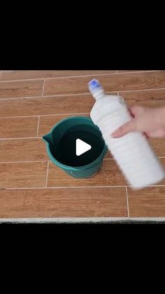 a person holding a plastic bottle over a trash can on the floor next to a toilet paper roll