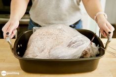 a woman holding a knife and fork in a roasting pan with a turkey wrapped in plastic