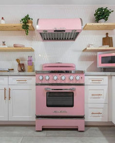 a pink stove top oven sitting in a kitchen next to white cupboards and shelves