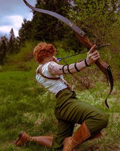 a woman with red hair is kneeling down and holding an arrow in her hand while aiming it at the viewer