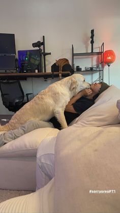 a man laying on top of a white couch next to a large dog in a living room