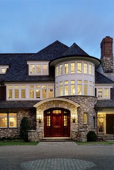 a large house with stone pillars and windows at night, lit up by lights on the front door