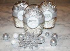 three glass jars filled with silver and white decorations on top of a marble countertop