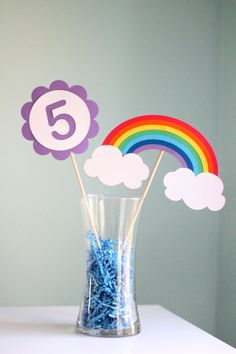 a vase filled with blue candies next to a rainbow and cloud topper on a table