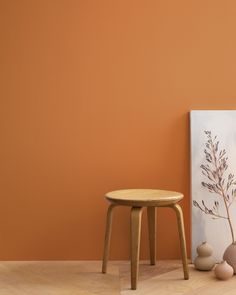 a small wooden stool next to a painting and vases on the floor in front of an orange wall