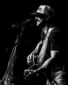 a black and white photo of a man singing into a microphone while playing an acoustic guitar