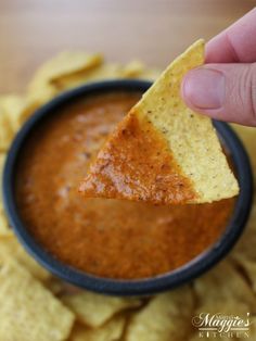 a hand holding a tortilla chip over a bowl of salsa