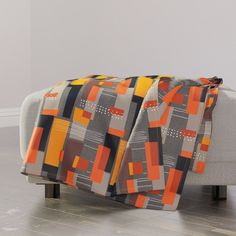 an orange and grey blanket sitting on top of a white couch next to a wooden floor