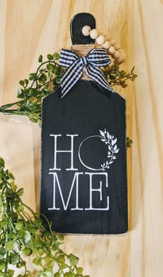 a sign that says home with a bow on it next to some greenery and beads