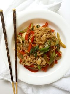 a white plate topped with noodles and vegetables next to chopsticks on a table