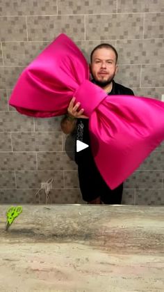 a man holding a large pink bow over his shoulder in front of a tiled wall