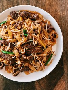 a white bowl filled with noodles and meat on top of a wooden table next to a fork