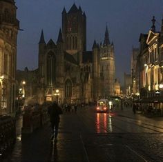 a city street at night with people walking and cars driving on the road in front of it