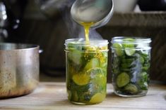 pickles being poured into jars on a wooden table