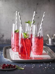 three glasses filled with red liquid and strawberries on a tray next to silver utensils