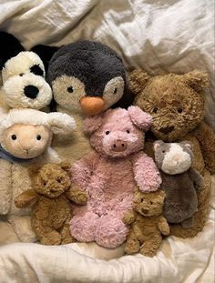 a group of stuffed animals sitting next to each other on a white bed sheet,