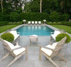 two lawn chairs sitting in front of a swimming pool surrounded by greenery and bushes