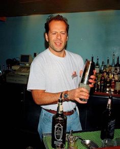 a man holding a bottle in his right hand while sitting at a table with bottles on it