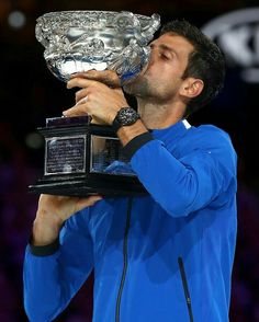 a male tennis player holding up a trophy and kissing the winner's glass bowl