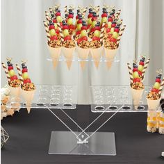 an assortment of fruit in ice cream cones on a clear display stand with black table cloth