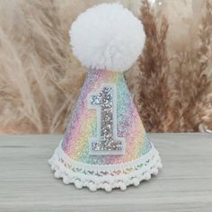 a small white hat with a rainbow number 1 on the front and a pom - pom at the bottom