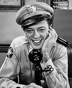 an old photo of a woman in uniform holding a telephone to her ear and smiling