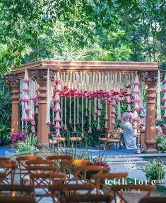 a man sitting on a bench in front of a wooden structure with flowers hanging from it