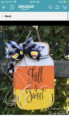 an orange, yellow and black fall is sweet sign hanging from a fence with leaves