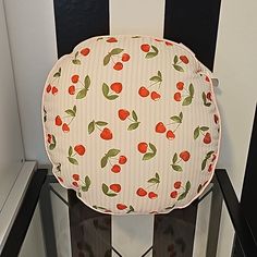 a round cushion with cherries on it sits in front of a black and white striped wall