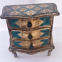 an ornately decorated chest of drawers with blue and gold paint on the top, against a white background