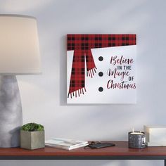 a christmas card hanging on the wall next to a table with a lamp and other items