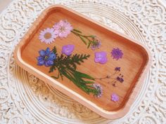 a wooden tray with flowers on it sitting on a lace doily covered tablecloth