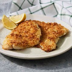 two pieces of chicken on a plate with lemon wedges