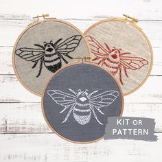 three cross stitch bee designs in different colors and sizes on a white wooden background with the text kit or pattern