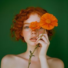 a woman with freckled hair holding two orange flowers