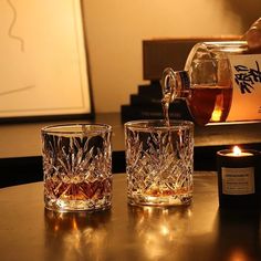 a person pouring whiskey into two glasses on a table