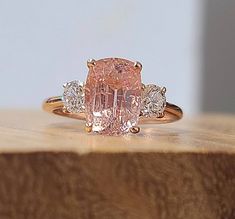 a pink diamond ring sitting on top of a wooden table with three diamonds around it