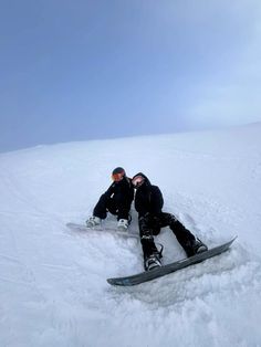 two snowboarders are sitting in the snow together