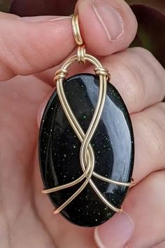 a person holding a black and gold pendant in their hand with it's wire wrapped around