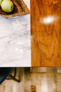 a wooden bowl with two green apples in it on top of a marble countertop