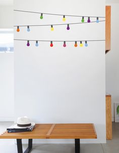 a wooden bench sitting in front of a white wall with colorful lights on the strings