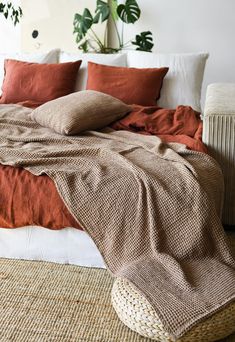 an unmade bed with pillows and blankets on top of it in front of a potted plant