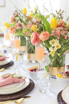 the table is set with plates, glasses and vases filled with flowers on it