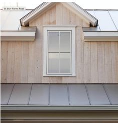 a window on the side of a house with shingled roofing and wooden siding